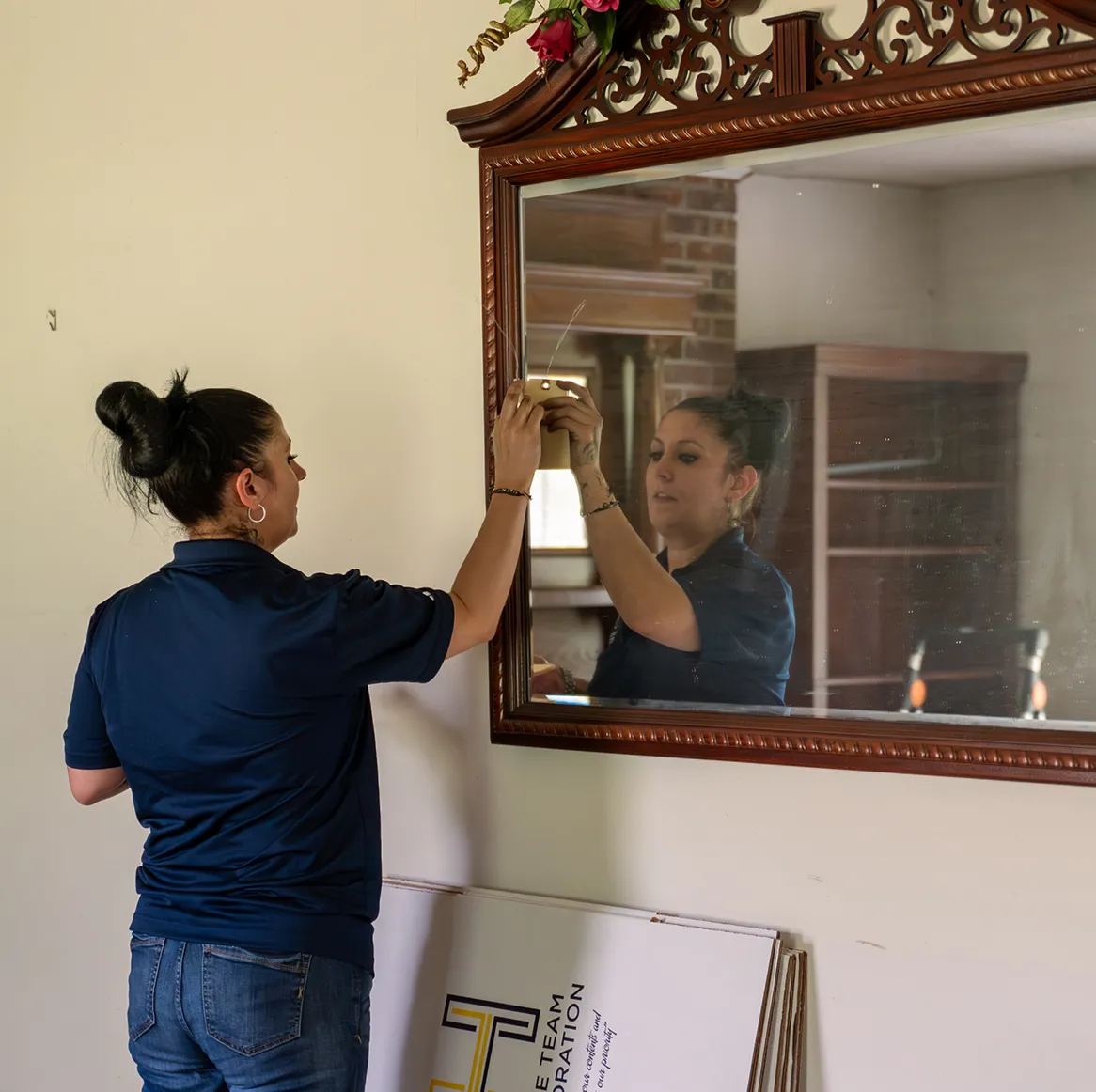 Person with tattoos and bun hairstyle cleaning a large decorative mirror with a cloth.