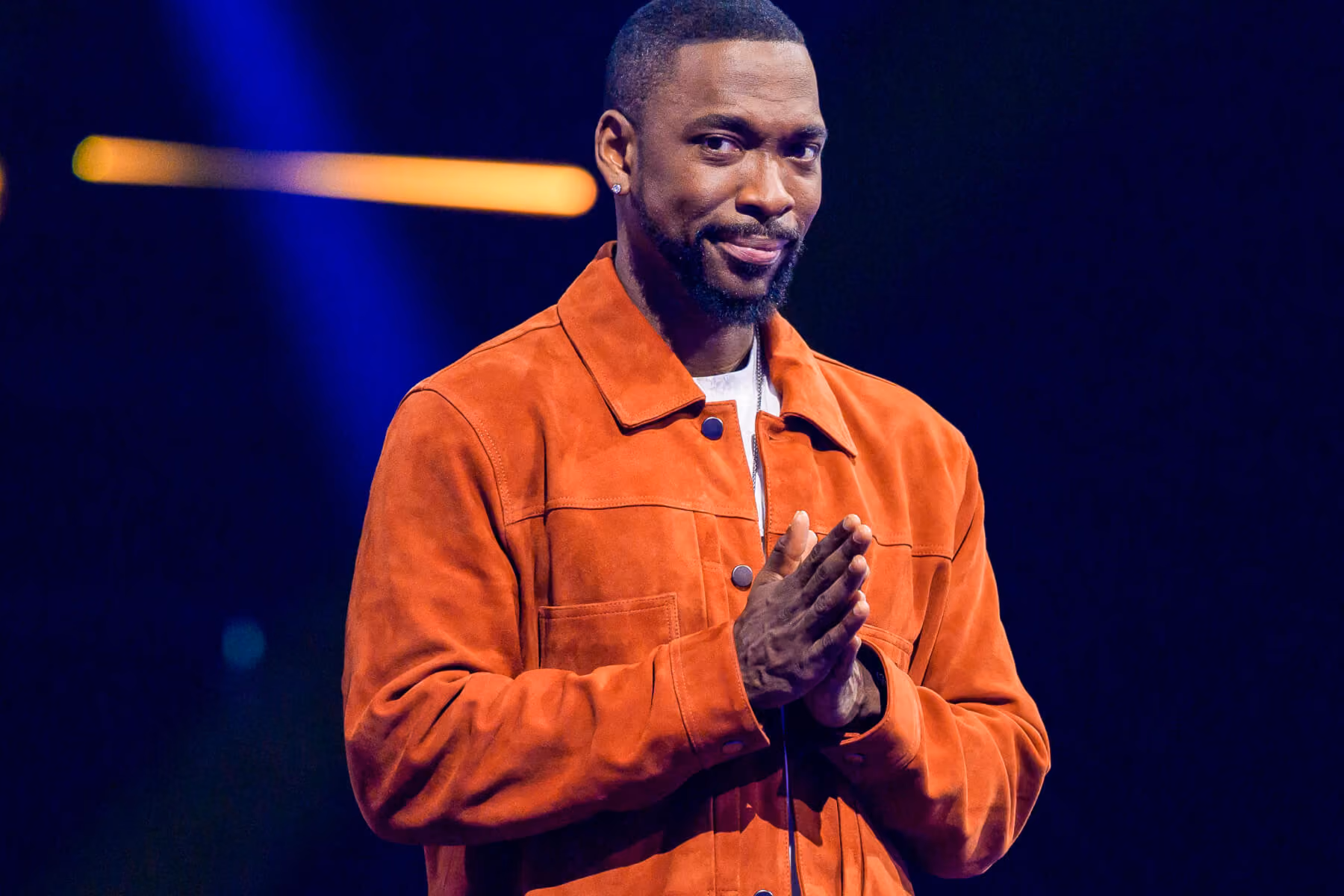 Host in an orange jacket smiles on stage