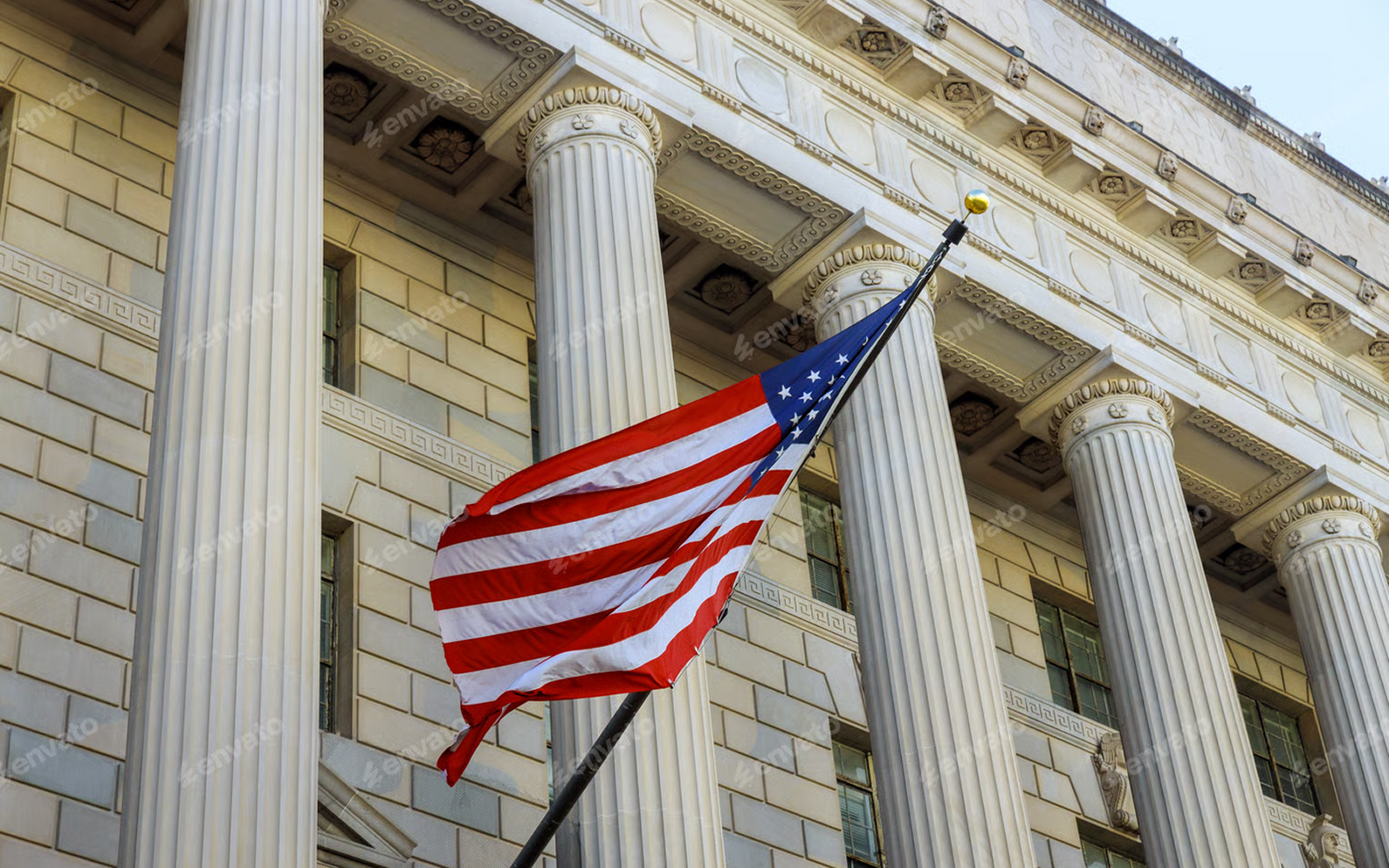 American flag waving on a pole in front of a neoclassical building with tall columns.