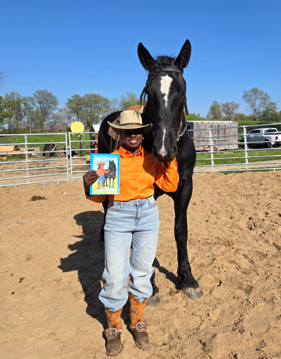 Queen Sabrina stands next to her colt, Solomon, recreating the cover of her book, which she holds in her free hand/