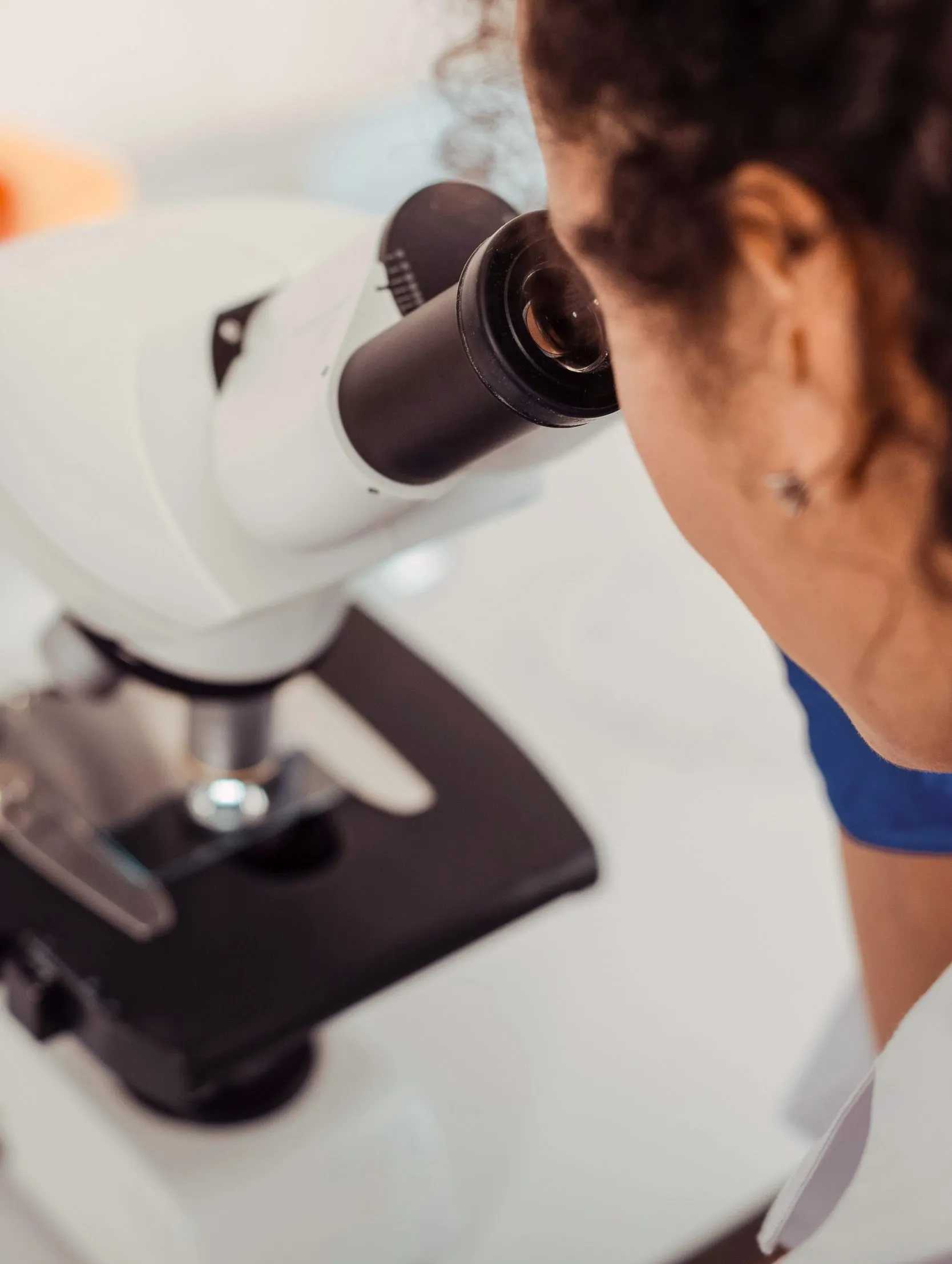 Person looking through the eyepiece of a white microscope in a lab setting.