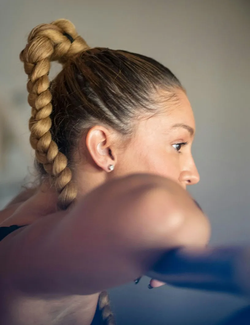 Close-up profile of a woman with a thick braided ponytail holding a barbell during a workout.