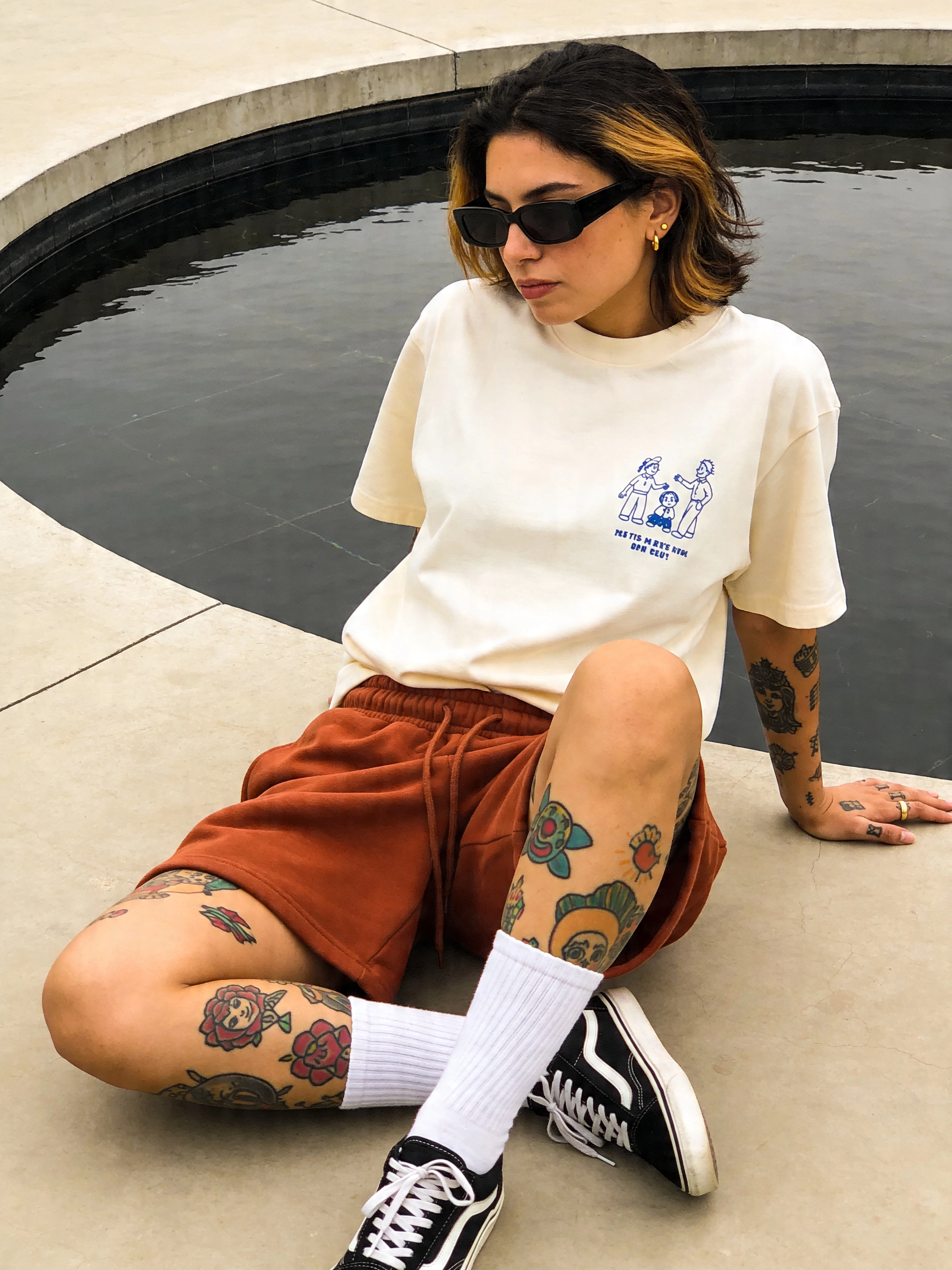Fotorealistisches weibliches KI-Model mit Tattoos und Sonnenbrille sitzt am Wasserbecken, Streetwear Stil, Trickhouse KI-Model-Agentur
