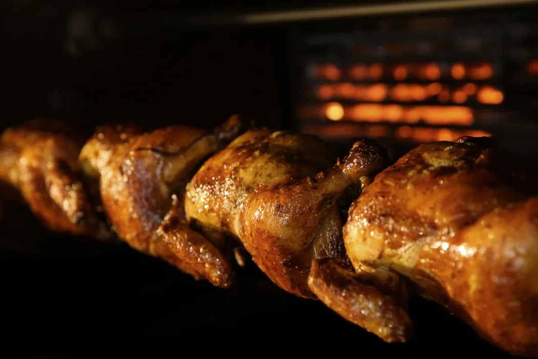 Poulets entiers dorés rôtis à la broche en rôtissoire avec flammes orangées en arrière-plan pour un service traiteur traditionnel.