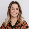 Portrait souriant d'une femme aux cheveux mi-longs balayage, blouse imprimee orange et noir, sur fond clair pour temoignage client.