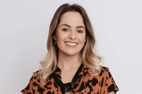 Portrait souriant d'une femme aux cheveux mi-longs balayage, blouse imprimee orange et noir, sur fond clair pour temoignage client.