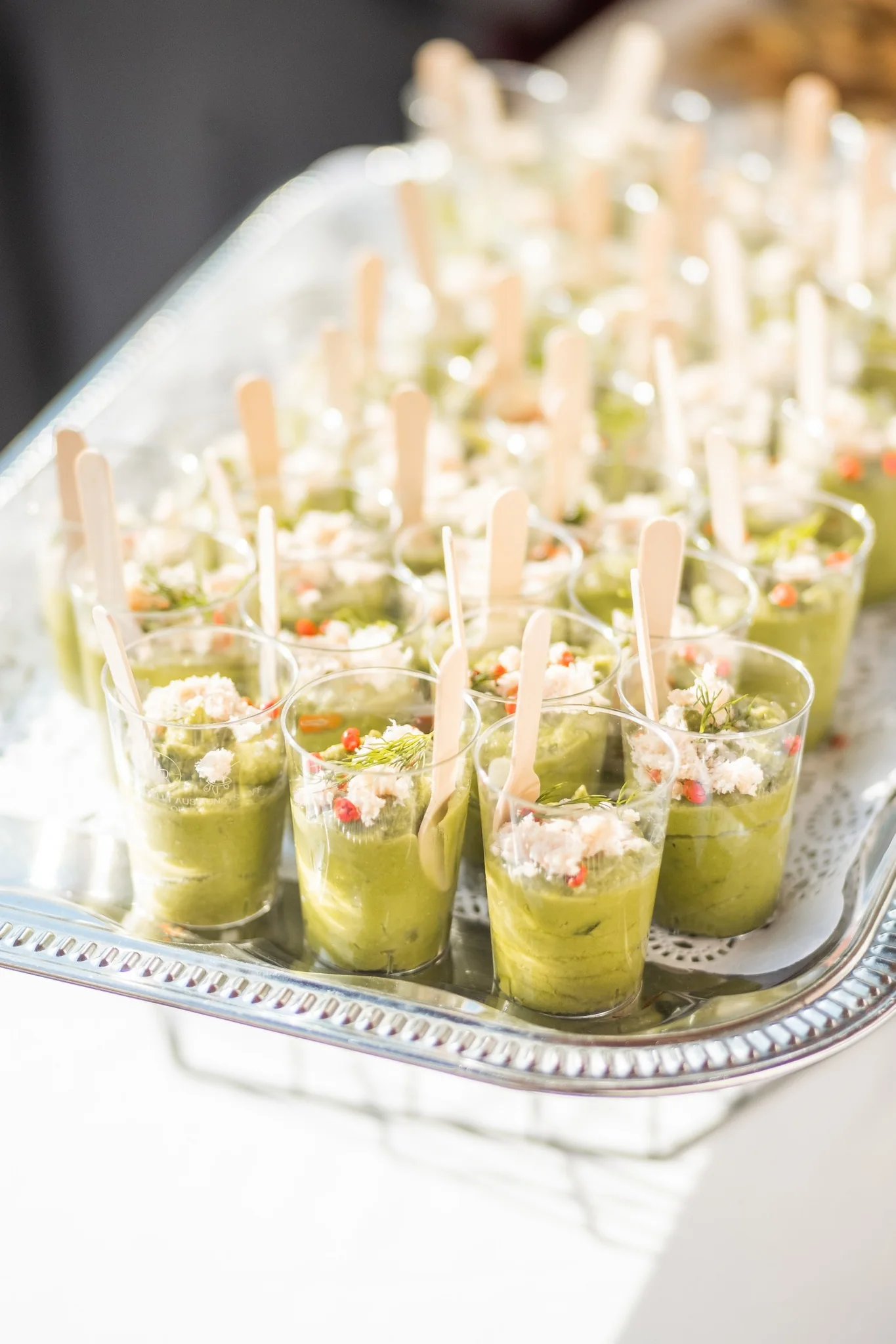 Plateau de verrines aperitives au guacamole, miettes de crabe, baies roses et aneth avec cuilleres en bois pour service cocktail dinatoire.
