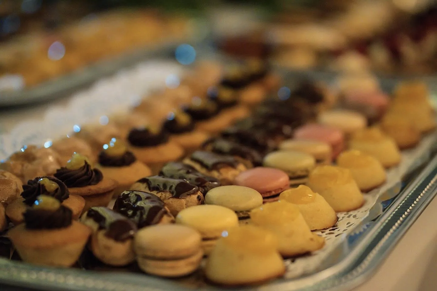 Plateaux argentés garnis de macarons colorés, éclairs au chocolat et mignardises sucrées pour buffet cocktail dinatoire raffiné.