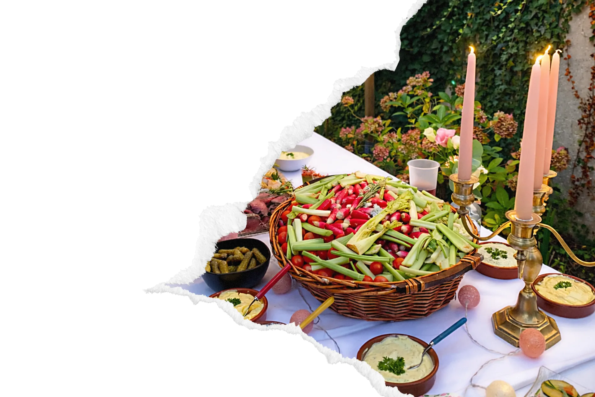 Buffet traiteur en extérieur avec corbeille en osier garnie de légumes croquants, houmous et charcuterie, dressé sous lanternes suspendues dans un jardin verdoyant.