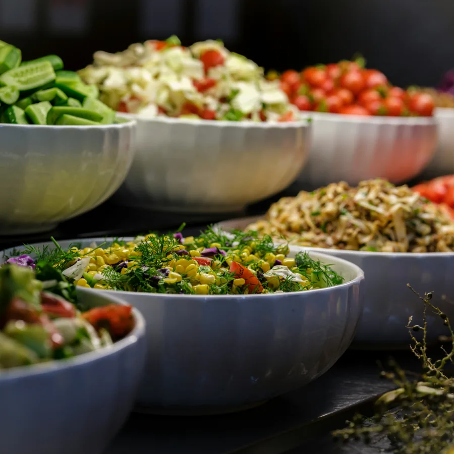 Bar à salades premium avec bols blancs alignés présentant salades composées variées (taboulé, légumes verts, tomates) sous éclairage chaud pour réception traiteur.