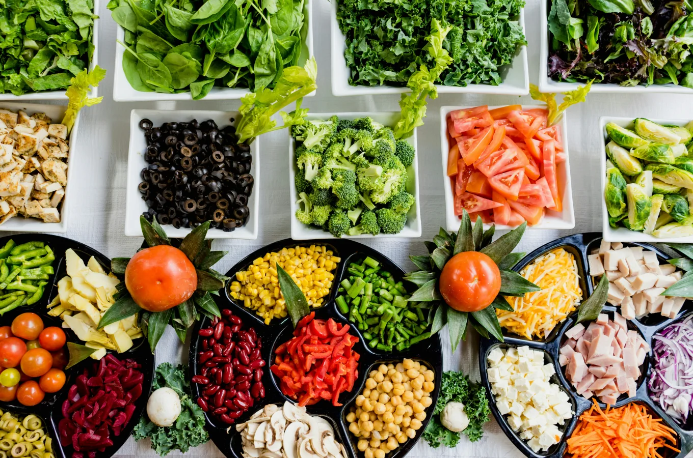 Vue de dessus d'un bar à salades complet à composer avec épinards, kale, brocolis, tomates, olives noires, maïs, haricots rouges, poivrons, fromage et jambon en bacs assortis.
