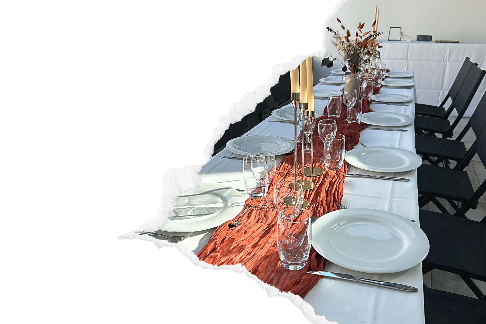 Longue table dressée avec assiettes blanches, verres à pied et chemin de table en gaze froissée terracotta, ponctuée de bougies dorées et d'un bouquet sec.