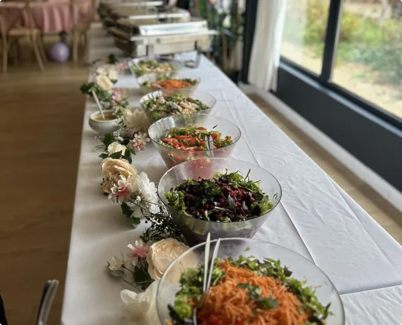 Buffet froid aligné de salades composées et plateaux de crudités présentés sur planches en bois face à une baie vitrée.