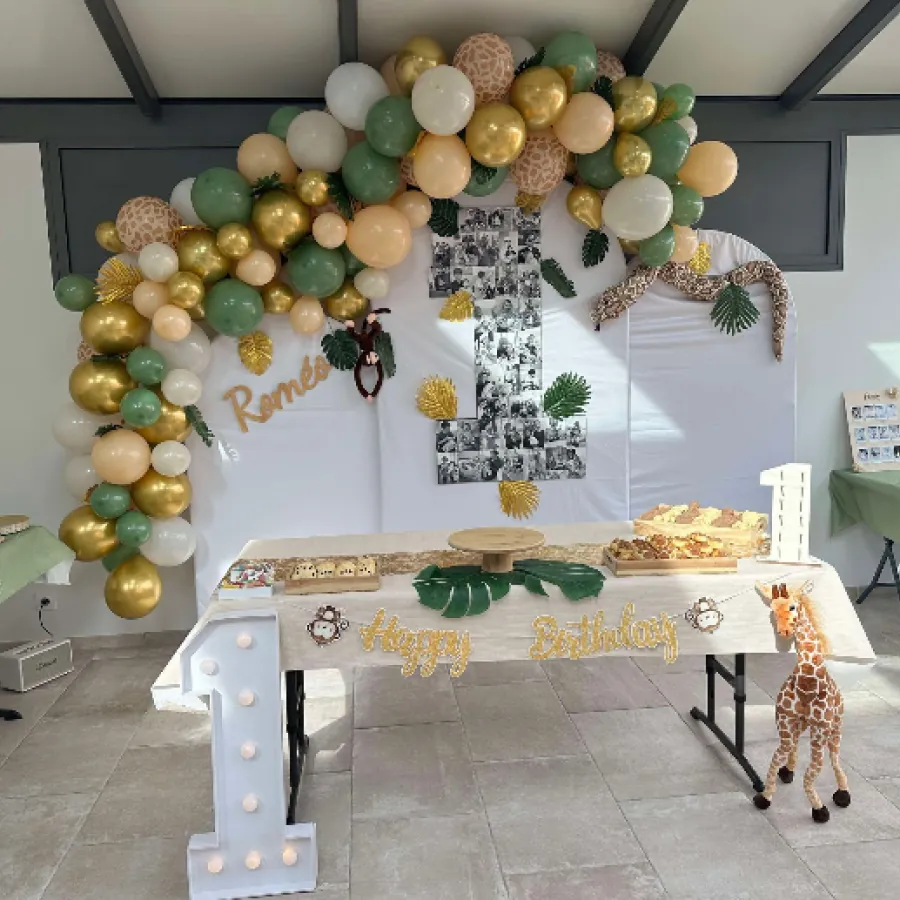 Decoration d'anniversaire dans une salle louee avec arche de ballons dores et verts, chiffre lumineux et thematique jungle pour un premier anniversaire.