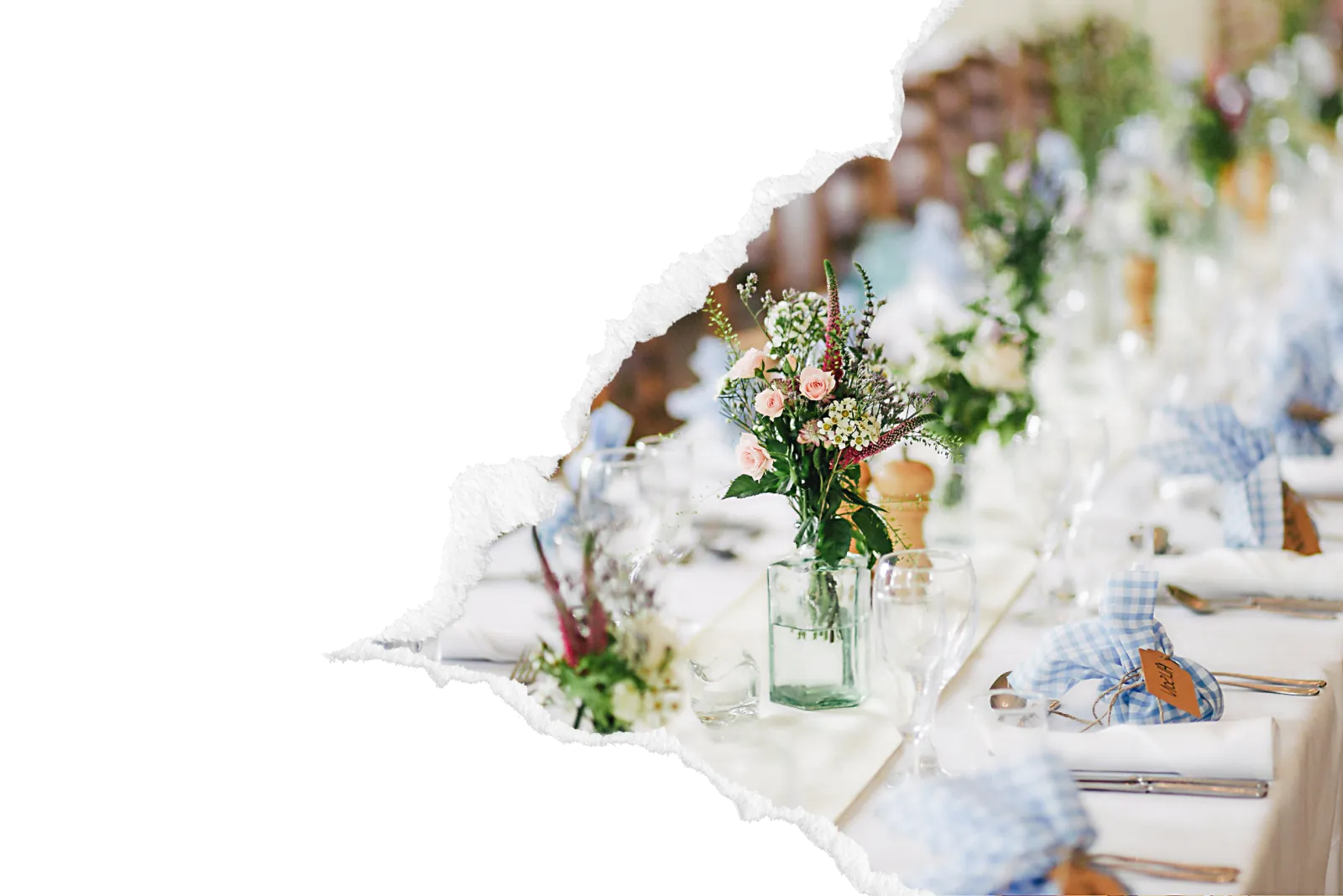 Table de mariage dressee avec bouquets champetres de roses et fleurs des champs, serviettes en vichy bleu nouees et verrerie, pour une reception traiteur dans la zone de Louviers. Image avec bord dechire decoratif.