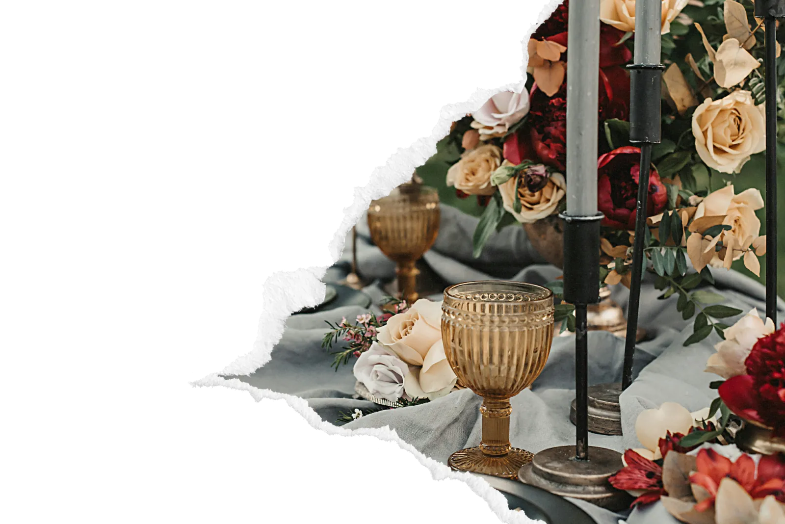 Table de mariage dressee avec roses crème et bordeaux, bougeoirs noirs et verre vintage dore sur nappe gris-bleu pour une reception elegante et intime dans la zone de Pacy-sur-Eure.