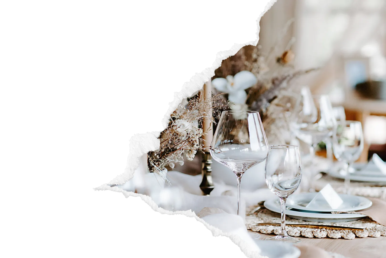 Table de mariage dressee avec verres a vin en cristal, bougie chandelier, composition de fleurs sechees et pampas, assiettes sur sets en rotin pour une reception elegante dans la zone des Andelys. Image avec bord dechire decoratif sur fond noir.