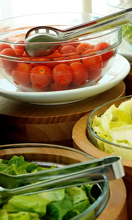 Bols en verre garnis de tomates cerises et de salades fraîches, disposés sur un buffet en bois pour un bar à salades convivial.