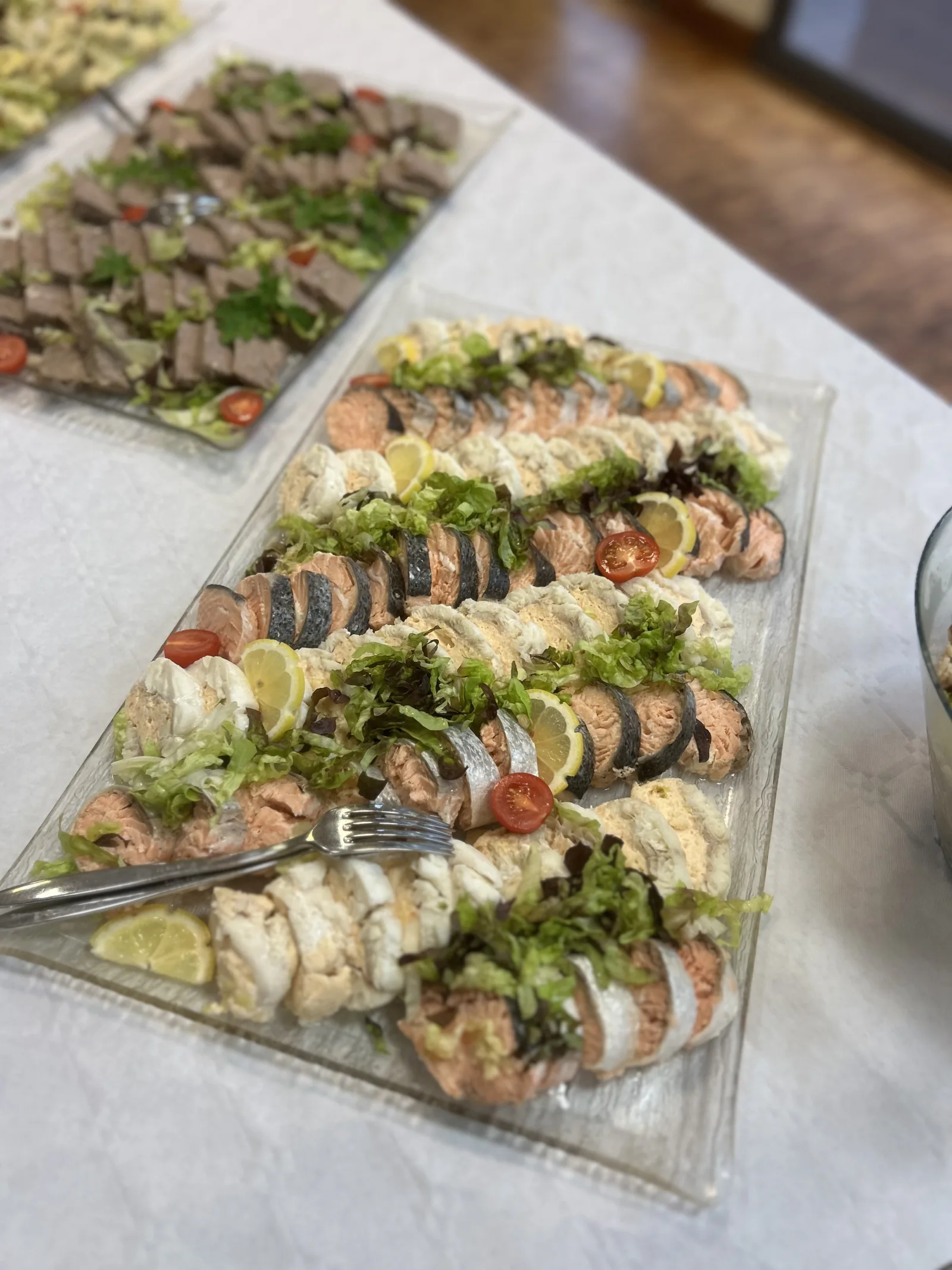 Plateau de saumon frais dressé en éventail avec rondelles de citron, salade verte et tomates cerises, accompagné d'un plateau de viande tranchée en arrière-plan.