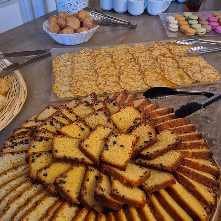 Plateau brunch traiteur : cake marbré tranché en éventail au premier plan, crêpes empilées, macarons colorés et beignets pour un buffet sucré convivial.