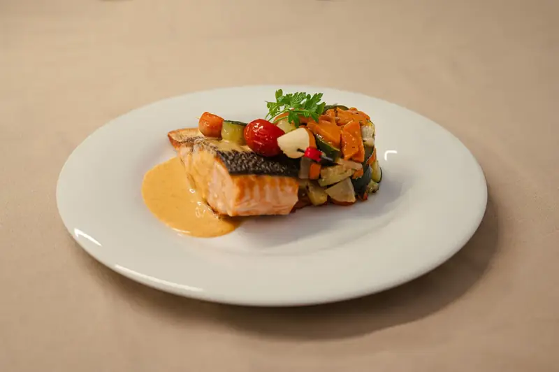 Pavé de saumon nacré accompagné d'une brunoise de légumes confits, brochette de garniture et sauce crémée — assiette signature À Votre Goût.