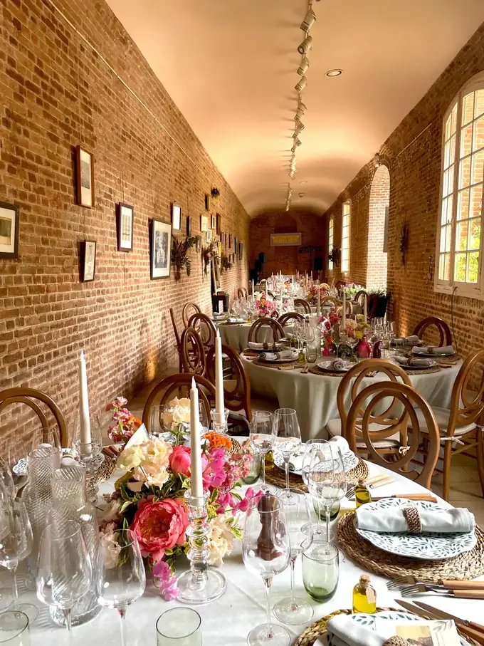 Salle de reception de mariage en orangerie brique avec tables rondes dressees, bouquets de pivoines colorees, chaises bistrot et nappes ivoire.