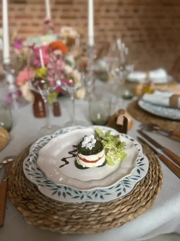 Entrée végétale dressée sur assiette en faïence, posée sur set tressé, dans une mise en scène florale aux chandeliers — réalisation événementielle À Votre Goût.