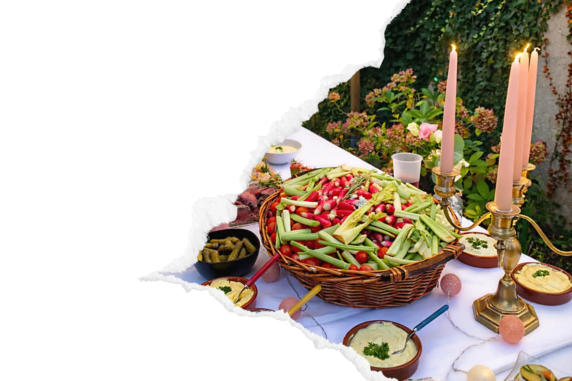 Buffet traiteur en extérieur avec corbeille en osier garnie de légumes croquants, houmous et charcuterie, dressé sous lanternes suspendues dans un jardin verdoyant.