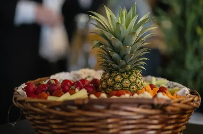 Corbeille en osier garnie de fruits frais découpés autour d'un ananas dressé en pièce centrale, présentation décorative pour buffet de réception.