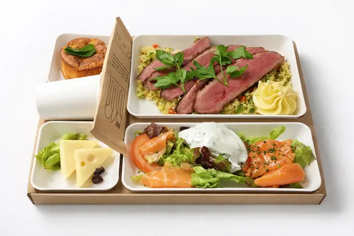 Plateau-repas gourmand livré en boîte carton, composé d'un rôti de bœuf tranché sur taboulé aux herbes, d'une entrée de saumon fumé avec salade verte et crème ciboulette, accompagné de fromage et d'un dessert brioché aux pommes.