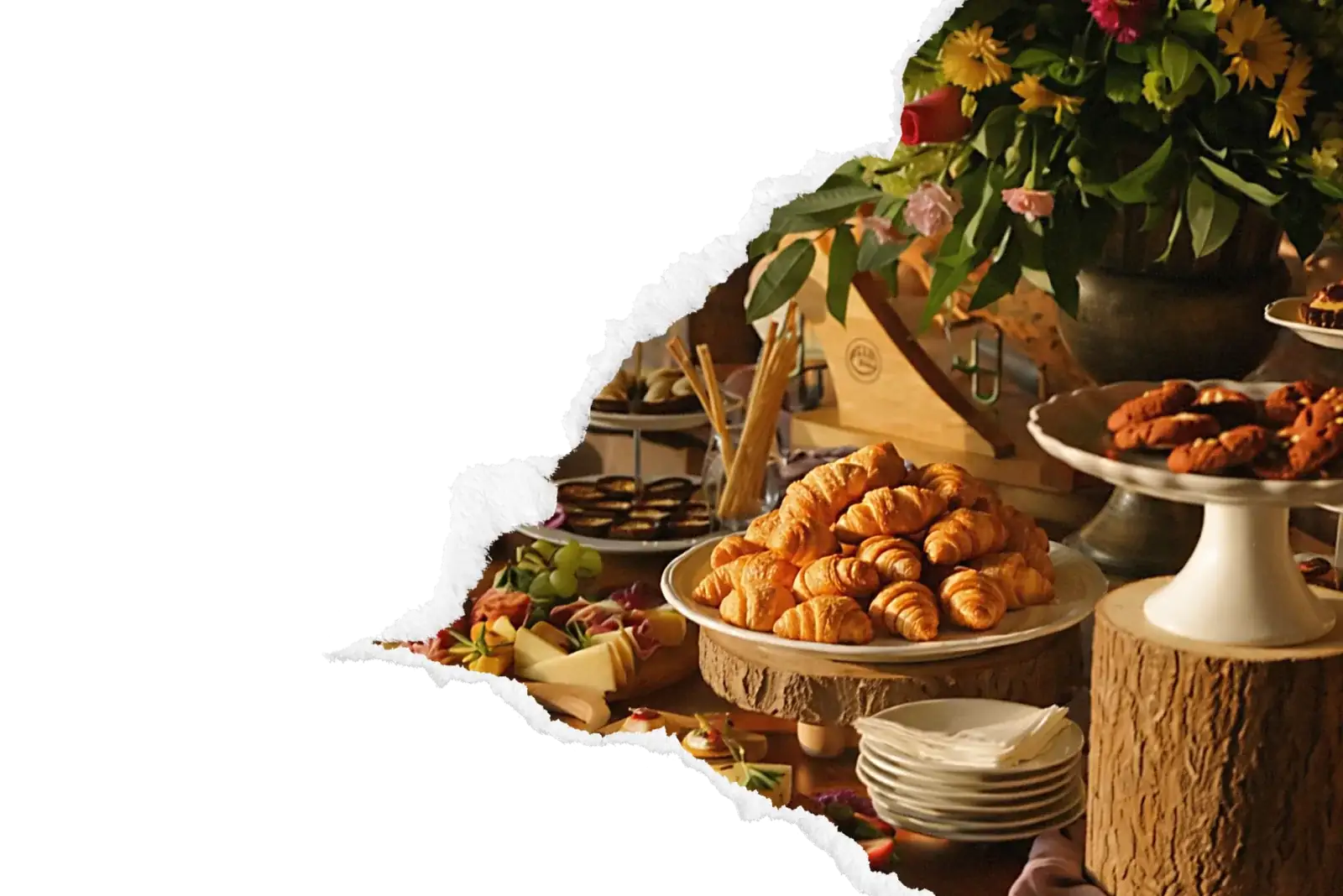 Buffet brunch composé de croissants dorés, planches de charcuterie et fromages, présenté sur des billots en bois avec bouquet de fleurs en arrière-plan.