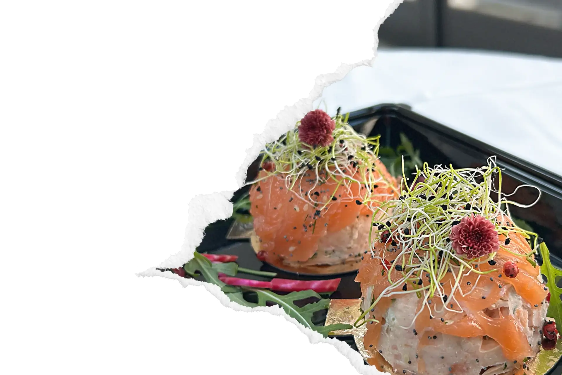 Tartares de saumon individuels garnis de pousses germees et fleurs comestibles, presentes en barquette de livraison sur lit de roquette, mis en valeur par un cadrage dechirure decorative pour le service de livraison de plats a la carte.