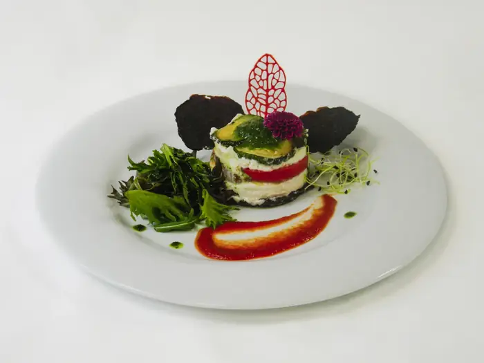 Entrée gastronomique dressée à l'assiette : millefeuille de légumes avec chips de betterave, mesclun, fleur comestible et coulis coloré.