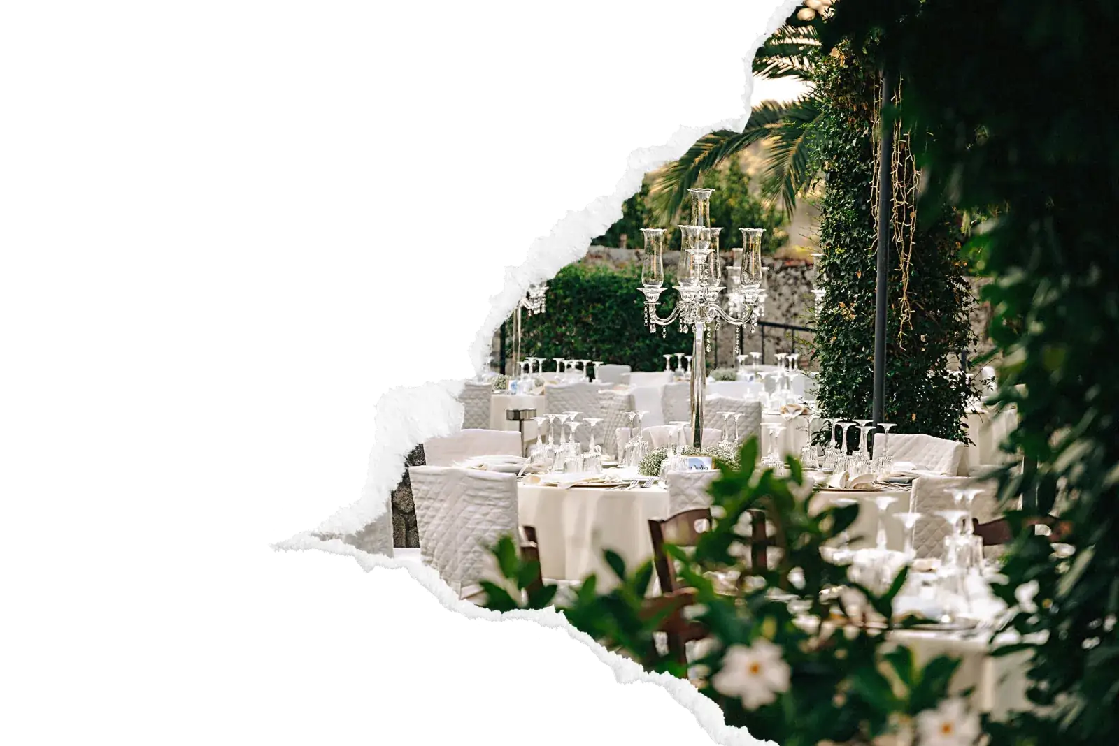 Reception de mariage avec tables elegamment dressees en nappage blanc, candelabres en cristal et chandelles, sous une tonnelle de jardin verdoyante avec palmiers et vegetation luxuriante pour une reception en exterieur dans la zone de Mantes-la-Jolie. Image avec bord dechire decoratif sur fond noir.