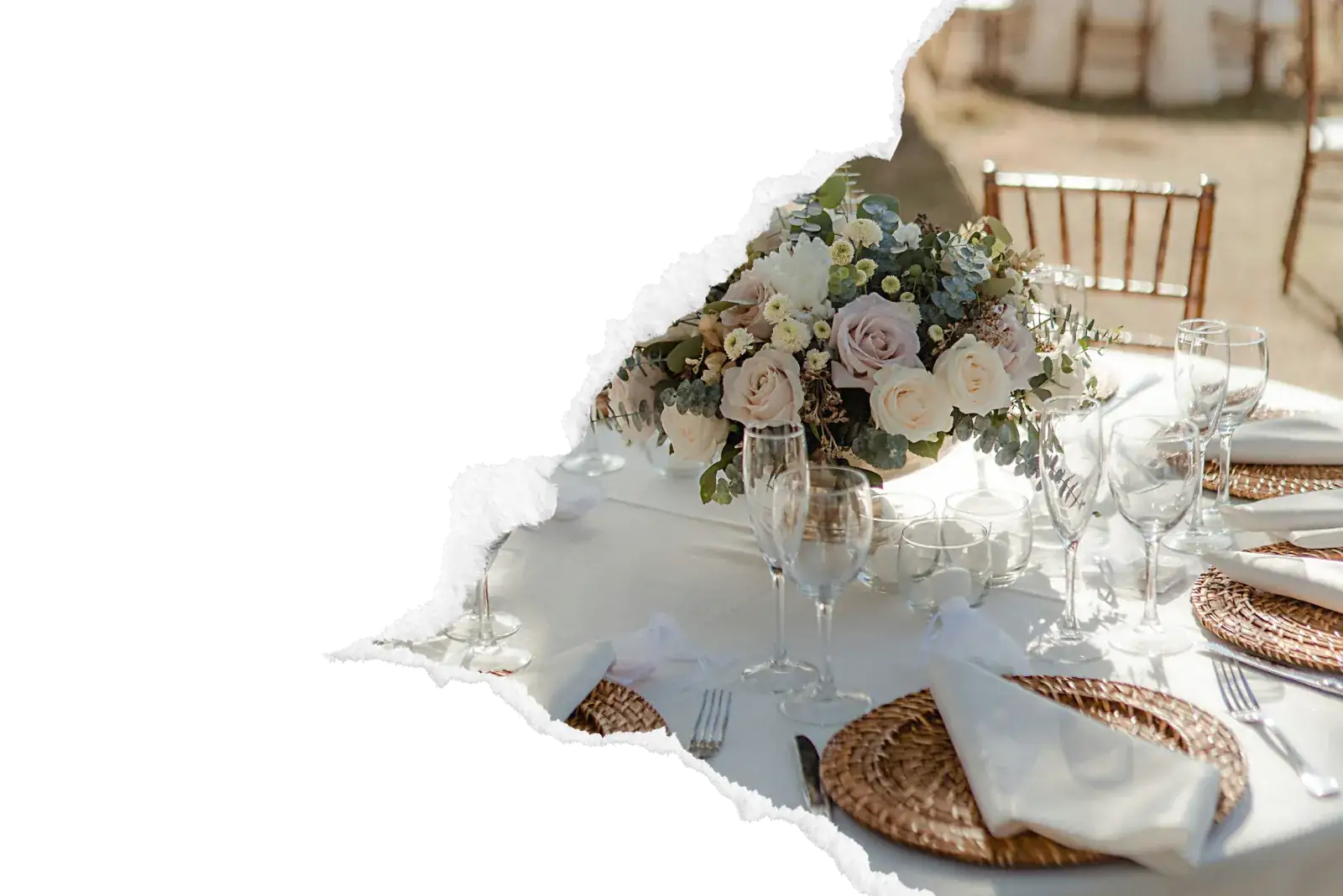 Table de mariage dressee en exterieur avec bouquet de roses pastel creme et rosees, verres en cristal, sous-assiettes en osier tresse et nappage blanc immaculé pour une reception elegante par le traiteur A Votre Gout dans la zone de Gisors. Image avec bord dechire decoratif sur fond noir.