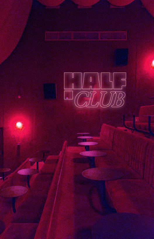 Intérieur d'un club avec des banquettes rouges, petites tables rondes et un mur avec enseigne lumineuse indiquant 'HALF CLUB'.