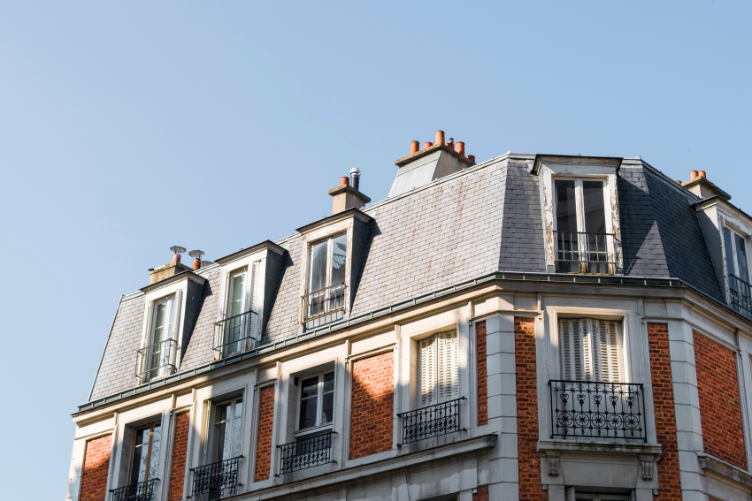 Façade d'un immeuble en pierre et briques avec des fenêtres mansardées et balcons en fer forgé sous un ciel bleu.