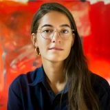 Young woman with long hair and glasses wearing a dark shirt against a red background.