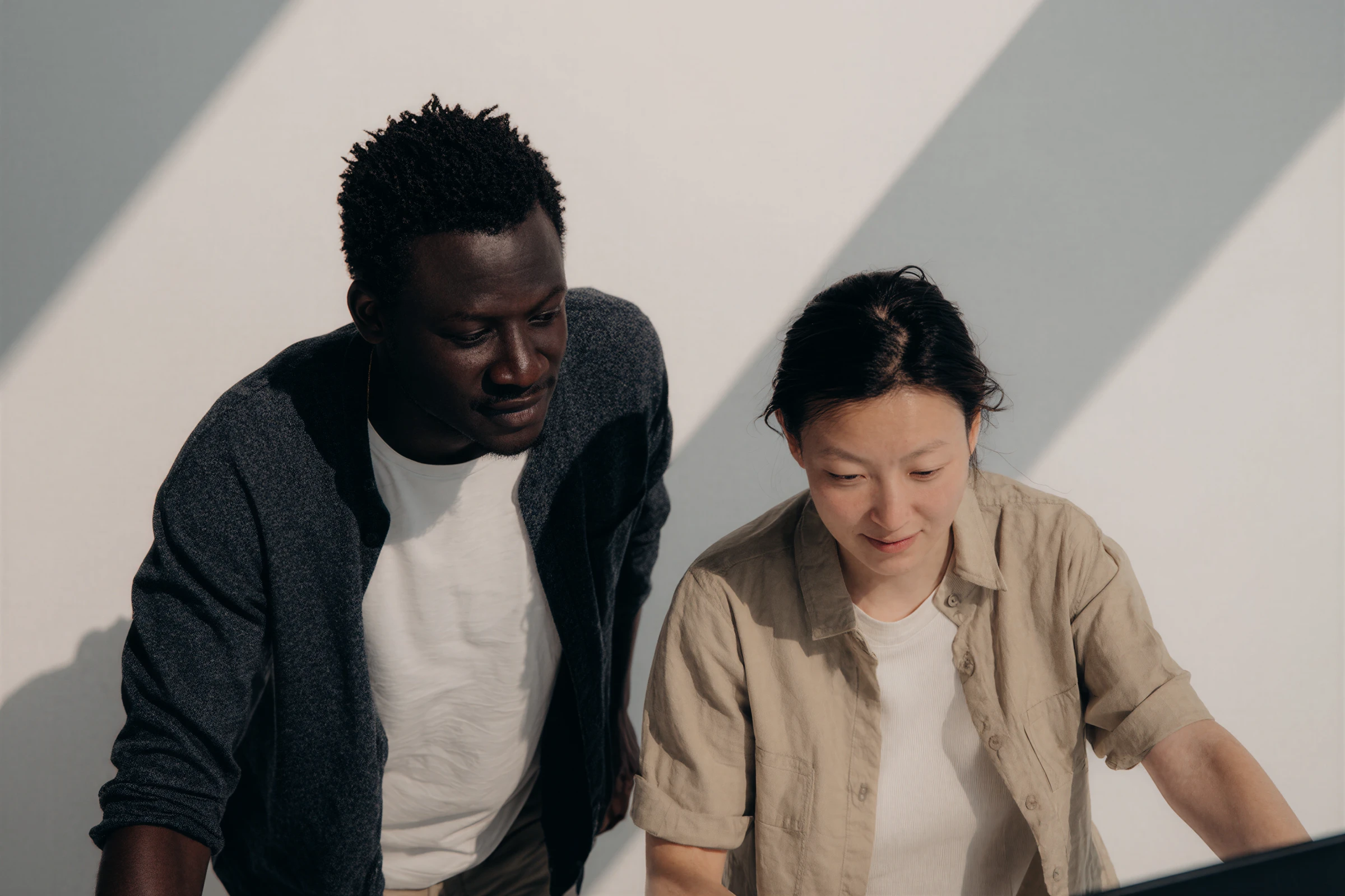 Two people focused and looking at a screen, one standing and one sitting in natural light.