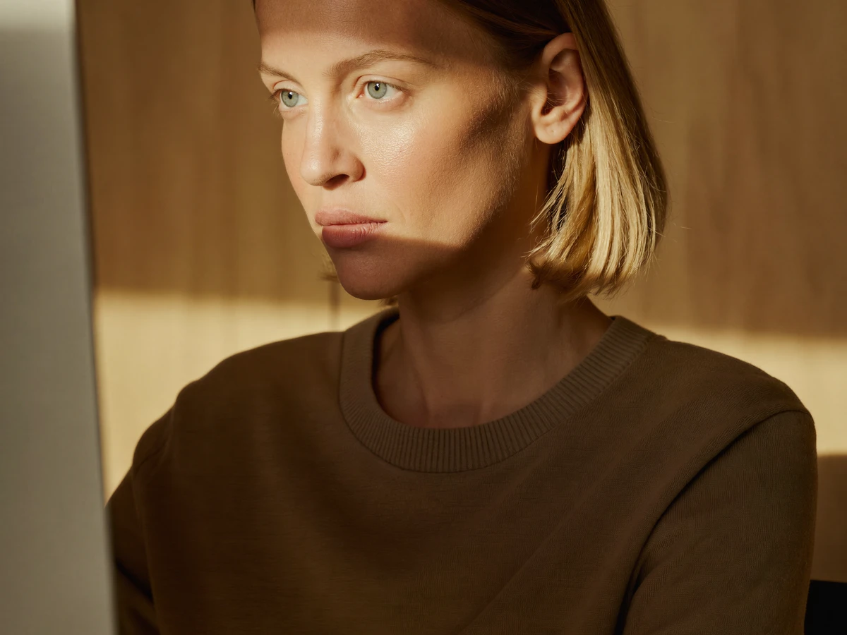 Woman with short blonde hair looking intently at a screen in warm, soft light.