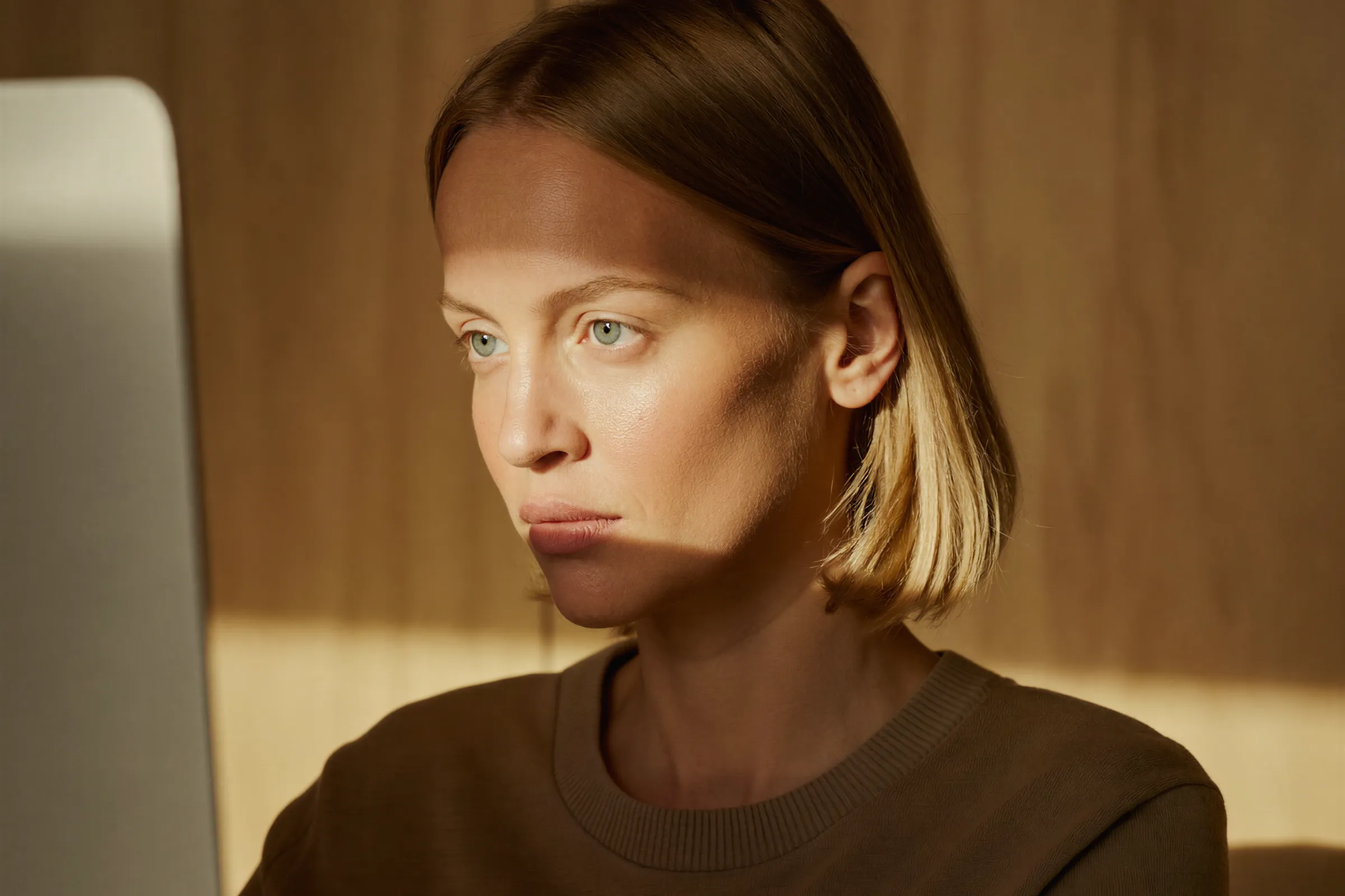 Woman with short blonde hair intently looking at a computer screen with sunlight on her face.