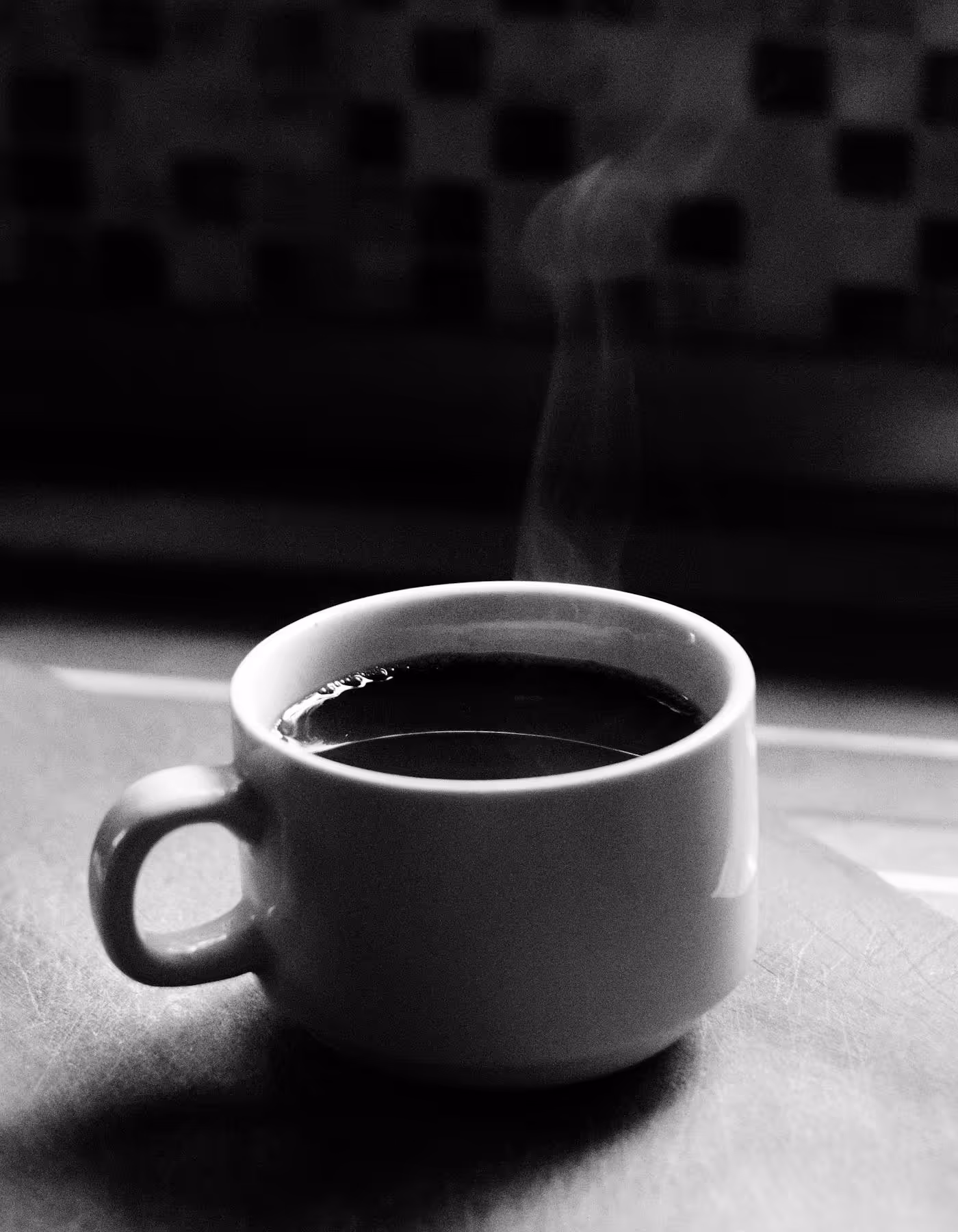 A single glass cup of dark coffee placed on a reflective surface
