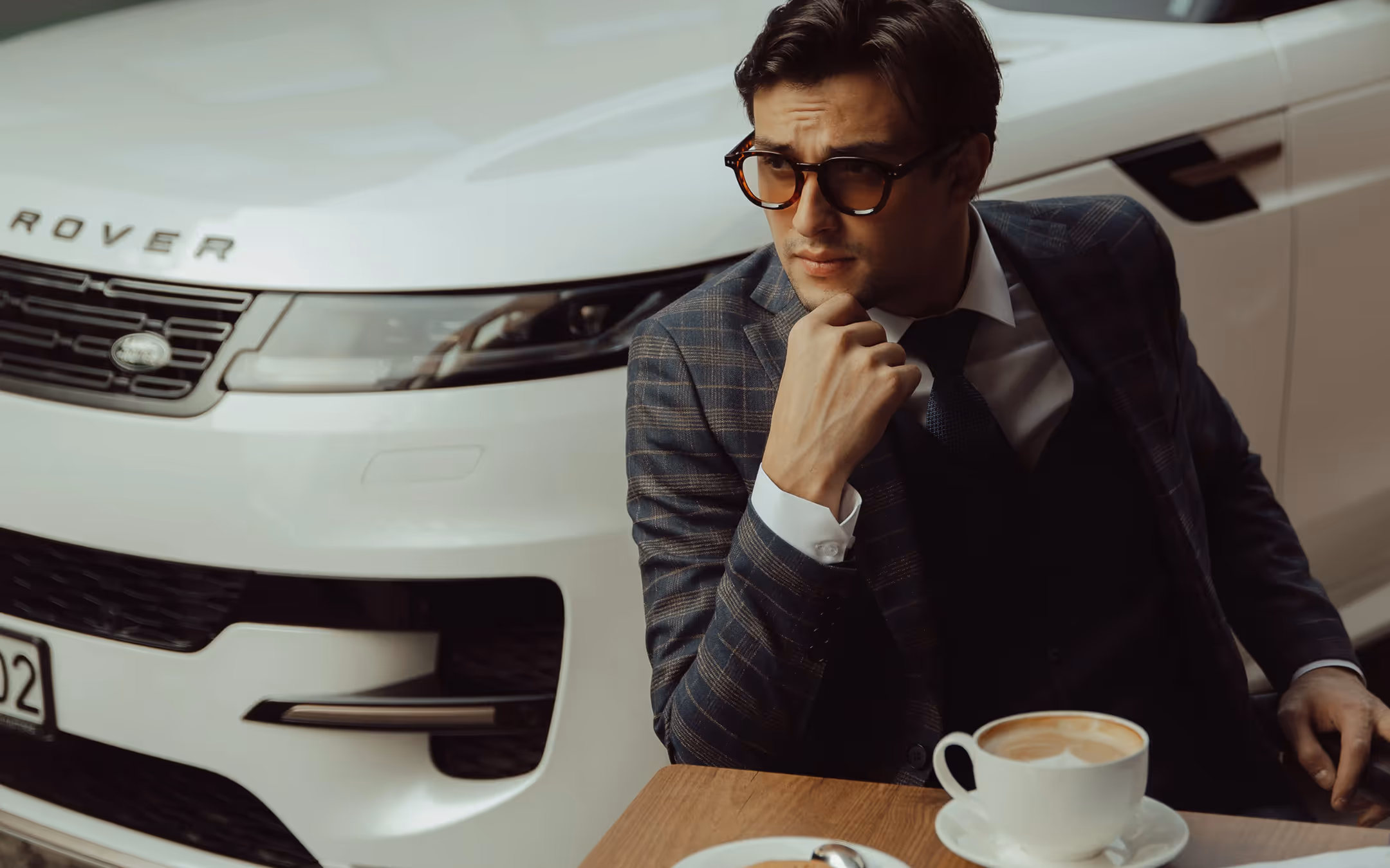 Элегантный мужчина в костюме сидит и пьет кофе перед Land Rover Sport