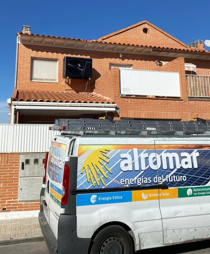 Dos trabajadores con cascos blancos y chalecos de seguridad instalando paneles solares en un techo mientras usan un ordenador portátil.