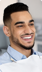 Smiling man with dark hair and beard wearing a light blue shirt and a white dental bib.