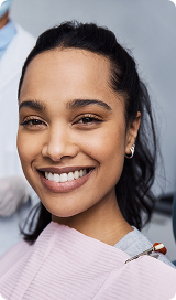 Smiling woman with dark hair in a dental bib during a dental visit.