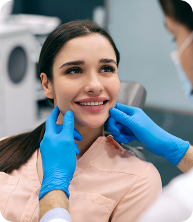 Dentist wearing blue gloves examining a smiling woman's face in a clinic.