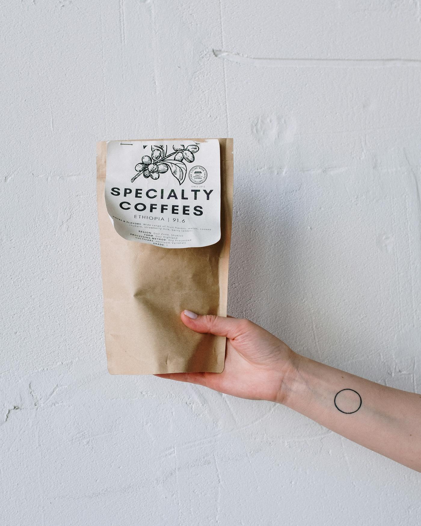 A hand holding a minimalist specialty coffee package against a soft wall