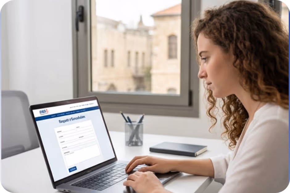Woman filling out an online request form on a laptop at a desk by a window with city buildings outside.