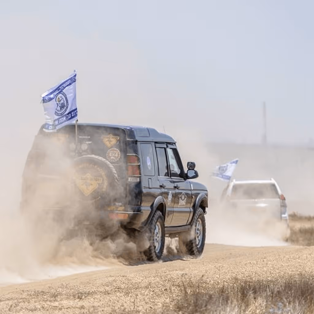 Two off-road SUVs driving on a dusty dirt road with flags attached to their rear sides.
